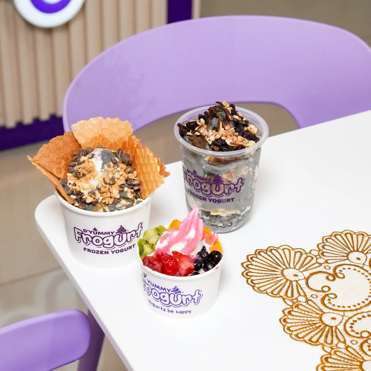 Three D'Yummy Frogurt cups with fruit, cereal, and waffle toppings